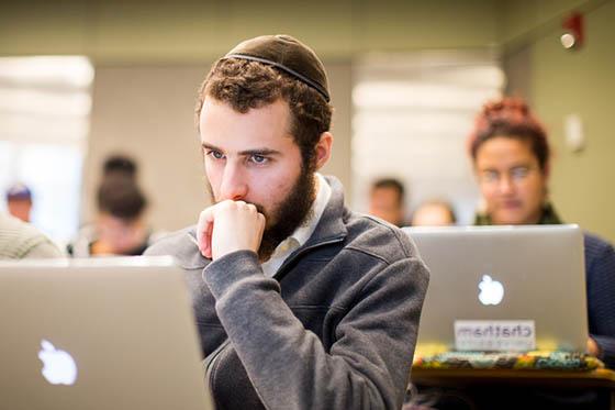 Photo of a male student in a yarmulke, 坐在2024欧洲杯官方投注的演讲厅里，看着他的电脑